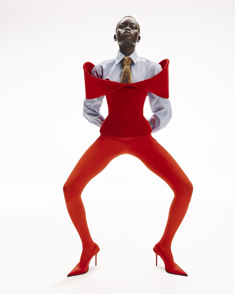 Fashion editorial shot of an African woman in red tights, red heels, a red bodice, and a striped shirt against a white backdrop.