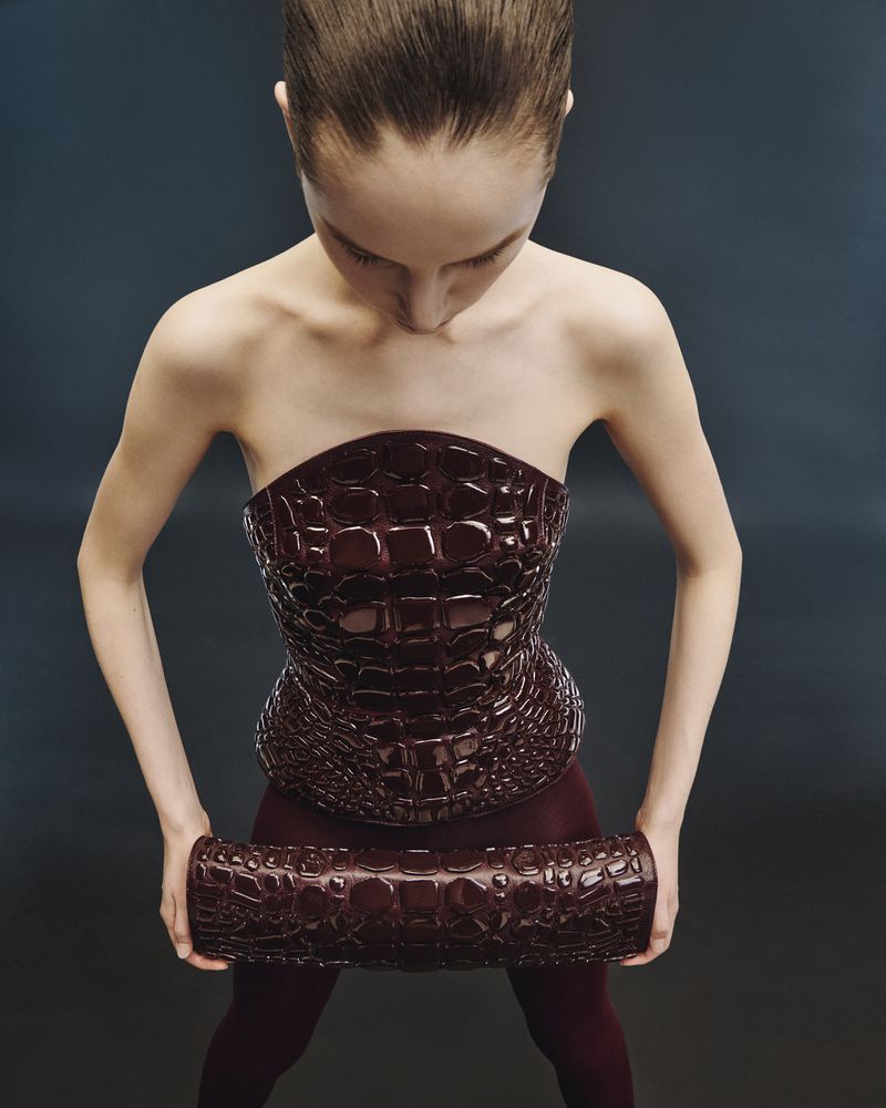 Woman in a brown faux-crocodile-skin strapless top and tights, holding a matching clutch, shot from above against a dark background.