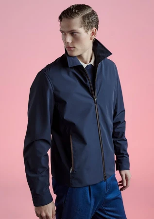 A male model wearing a dark navy zip jacket and blue trousers against a solid pink backdrop for Paul and Shark Spring Summer 25.