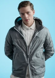 Model wearing a grey hooded jacket and white sweater against a light blue studio backdrop for Paul & Shark S/S 25.