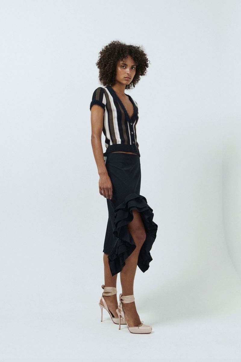 Model wearing a striped V-neck top and black ruffled skirt against a white studio background
