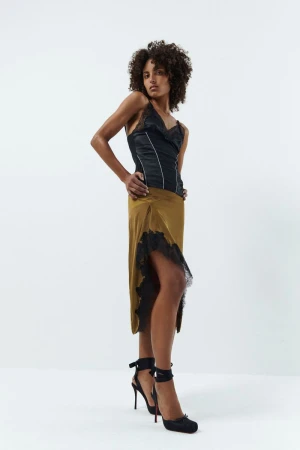 Model in a black satin top and olive midi skirt standing against a white seamless background for Vaillant Pre-Fall 25.