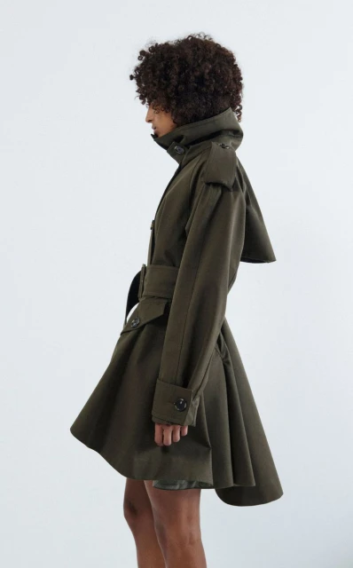 Profile of a woman wearing an olive green trench coat against a white backdrop, showcasing the garment's fit and design.