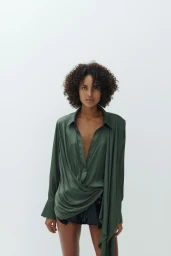 Model with dark curly hair wearing an olive green silk shirt against a white seamless background