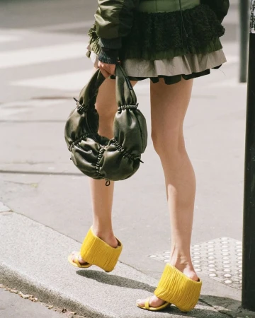 Eye-level shot of a person outdoors, wearing a green skirt, jacket, yellow platform sandals, holding a green handbag, on a city street.
