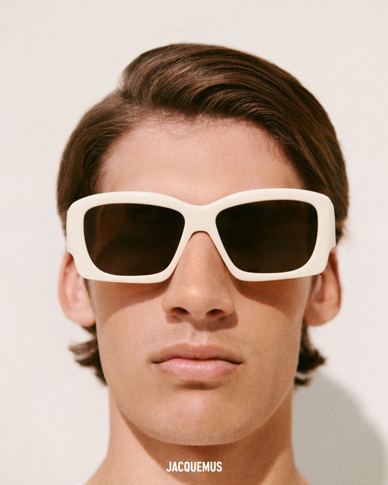 Close-up studio shot of an adult male wearing square off-white sunglasses with brown hair and light skin against a white background.