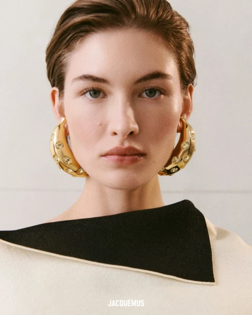 Close-up of a woman with short brown hair wearing a black and cream top and gold hoop earrings with crystals. Beauty shot.