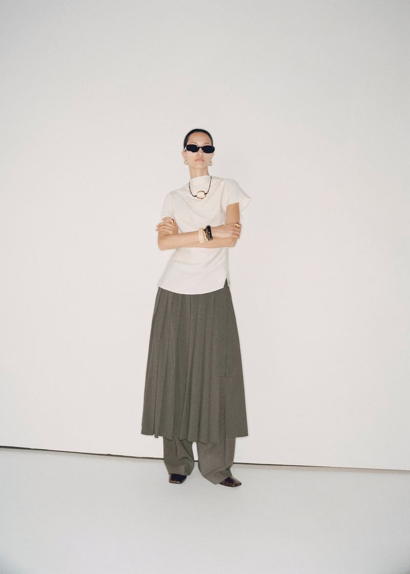 Fashion photography featuring an adult woman in a long skirt and t-shirt, posing in a full shot on a white seamless background.