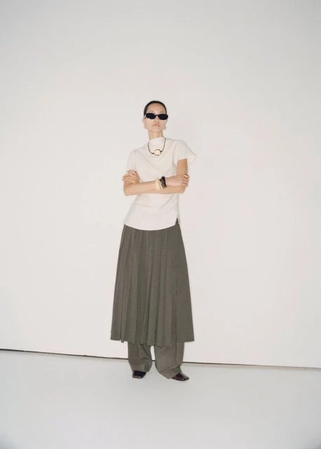 Fashion photography featuring an adult woman in a long skirt and t-shirt, posing in a full shot on a white seamless background.