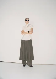 Model wearing sunglasses, white top, and olive skirt standing against a plain white studio wall for Mango America campaign.