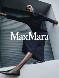 Model in a dark ribbed turtleneck and skirt posing dynamically against a building exterior with the Max Mara logo.