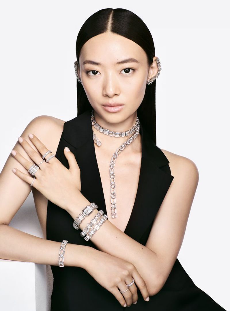 Asian woman in elegant pose wearing luxury jewelry, including rings, bracelets, necklace, and ear cuffs against a plain white background.