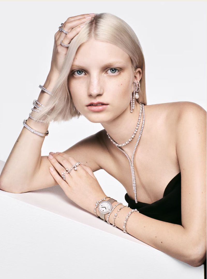 Blonde female model wearing crystal jewelry and wristwatch against white background for Swarovski