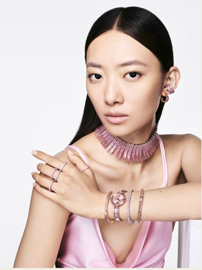 Glamorous Asian woman adorned with pink gemstone jewelry including a choker, earrings, rings, watch, and bracelets on a white background.