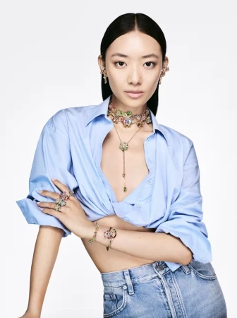 Elegant Asian woman posing indoors wearing a light blue shirt, jeans, and colorful jeweled jewelry in a beauty and fashion editorial.