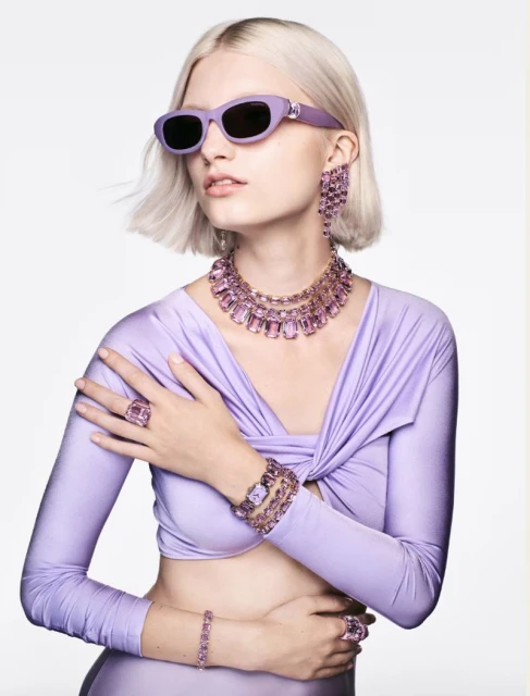 Fashionable woman in lilac outfit accessorized with statement jewelry: necklace, earrings, bracelets, rings and sunglasses.  