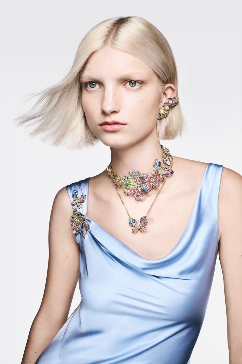 Model with blonde hair wearing a light blue satin dress and crystal floral jewelry against a white background