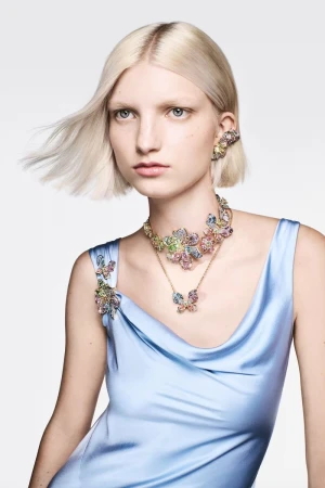 Model with blonde hair wearing a light blue satin dress and crystal floral jewelry against a white background
