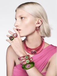 Close-up portrait of a blonde model wearing pink and green crystal jewelry and a pink dress against a white background