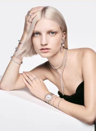 Blonde female model wearing crystal jewelry and wristwatch against white background for Swarovski