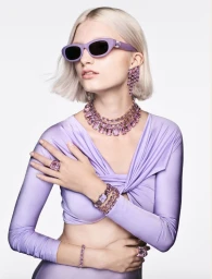 Model in lavender top wearing purple sunglasses and crystal jewellery against a white backdrop