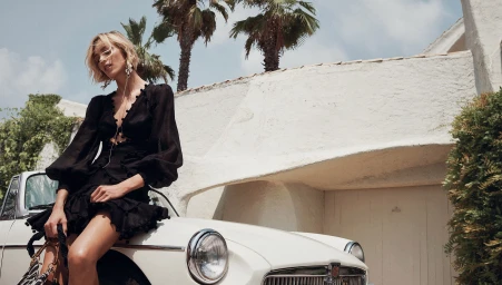Model Anja Rubik wearing a black dress leaning on a vintage white car for Zimmermann Resort RTW