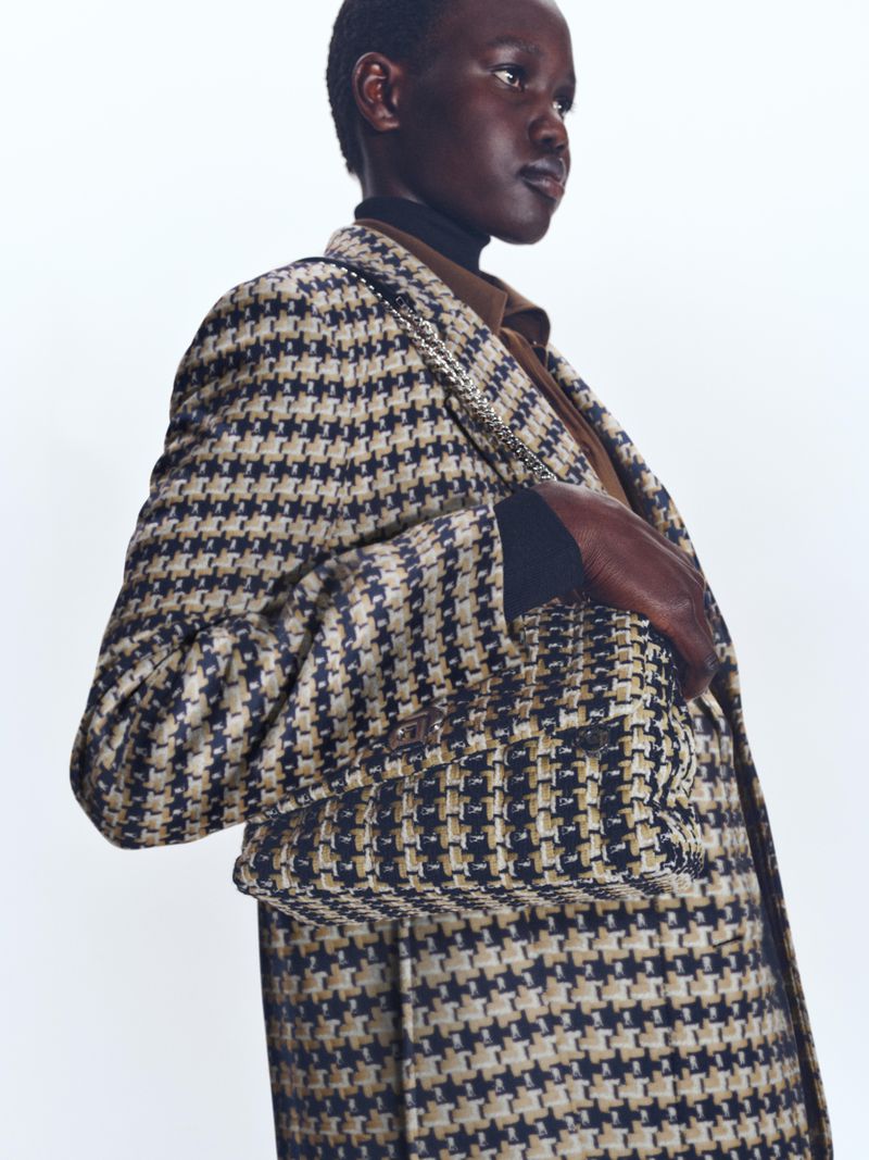Fashionable woman wearing a houndstooth blazer and brown turtleneck against a white backdrop in a studio setting.