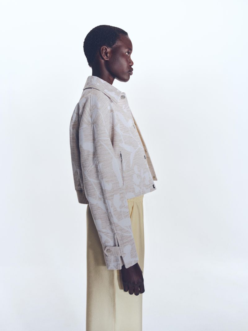 Model in profile wearing a patterned jacket and light trousers against a seamless white background for BOSS Spring 2025 Womenswear