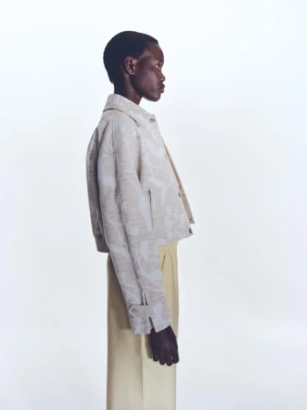 Model in profile wearing a patterned jacket and light trousers against a seamless white background for BOSS Spring 2025 Womenswear