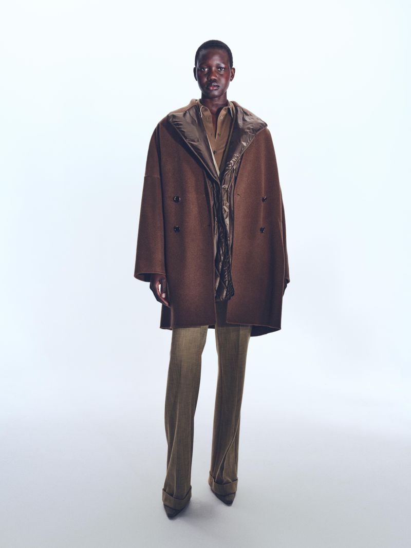 Model standing against a white seamless backdrop wearing a brown coat and trousers for BOSS Spring 2025 Womenswear.