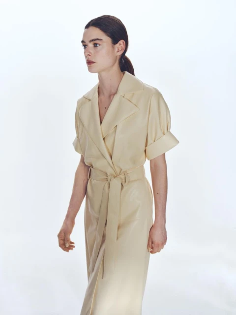 Elegant woman in a cream-colored wrap dress poses in a bright studio. The portrait showcases a modern and minimalist fashion aesthetic.