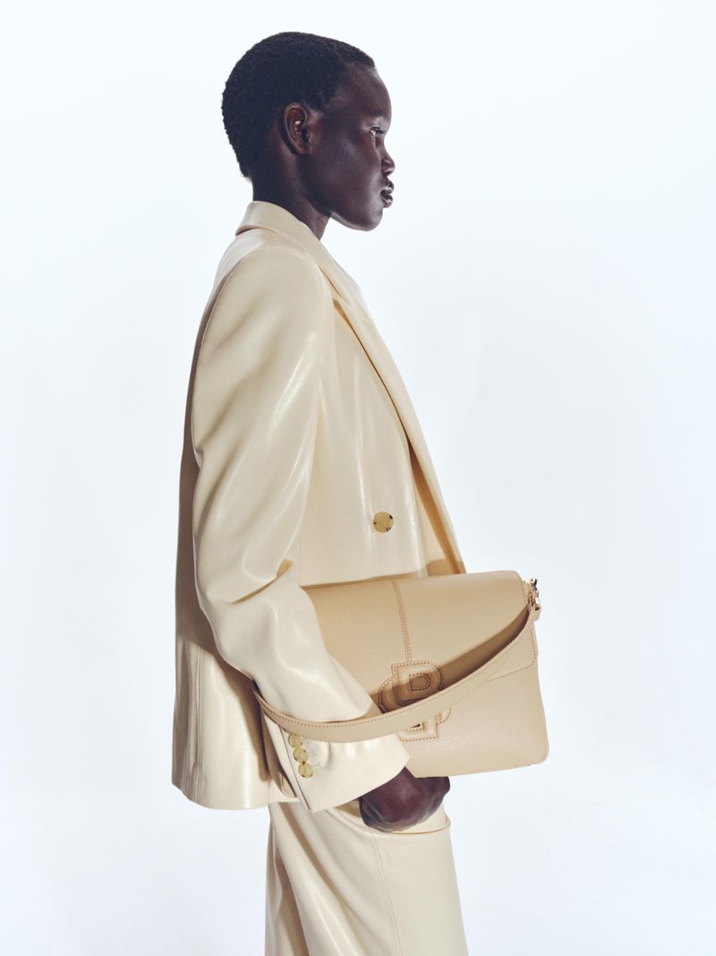 Model in cream blazer holding matching shoulder bag against white studio background for BOSS campaign