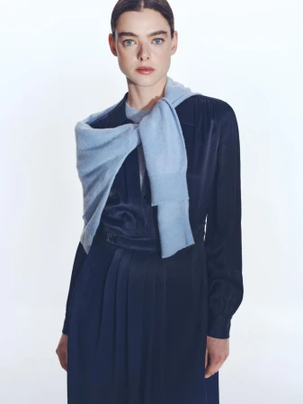 Model in dark blue dress wearing a light blue sweater tied around shoulders against a white background