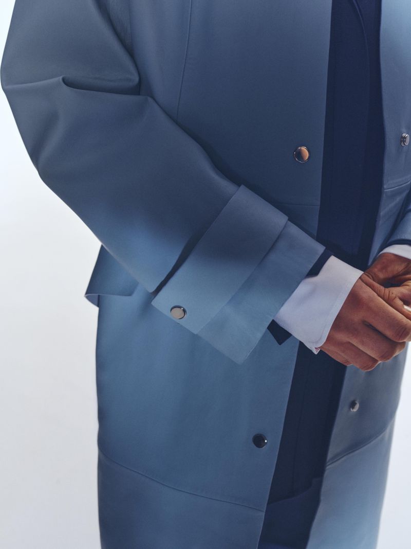 Fashion shot featuring a torso view of a person in a blue-grey gradient jacket with silver buttons and a white shirt on a white background.