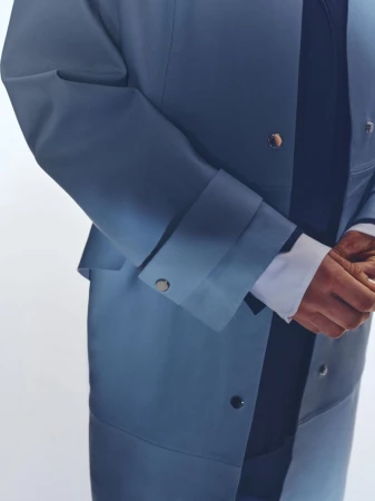 Fashion shot featuring a torso view of a person in a blue-grey gradient jacket with silver buttons and a white shirt on a white background.
