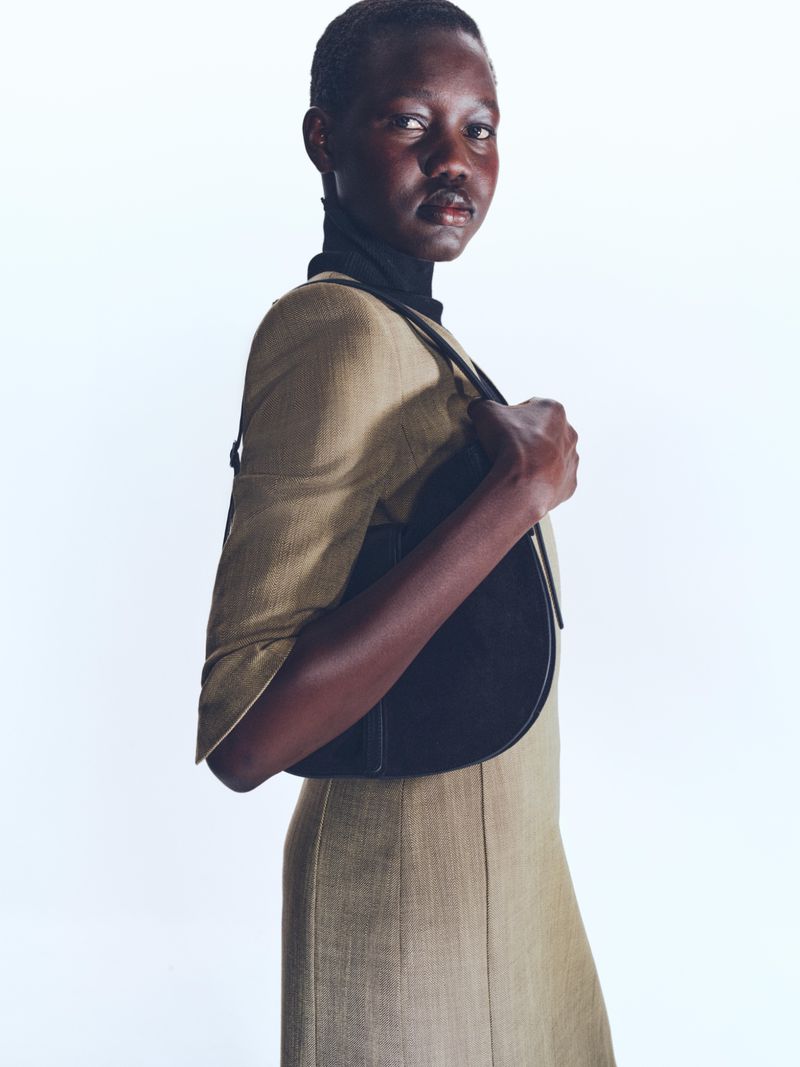 Model in a tan dress and black handbag against a white background for BOSS Spring 2025 Womenswear