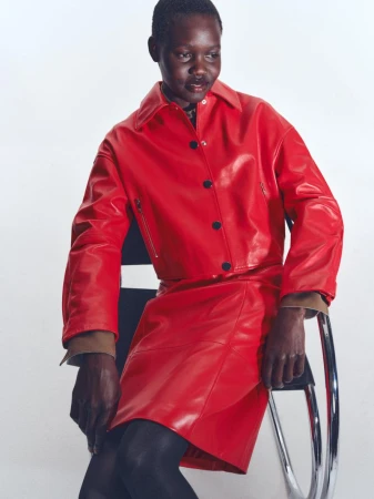 Model wearing a red leather jacket and matching skirt seated on a chrome chair against a white background for BOSS