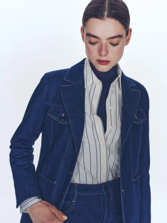 Model wearing a blue denim jacket over a striped shirt and dark blue turtleneck against a white background.