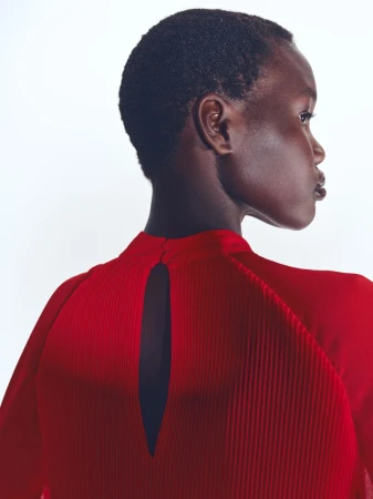 Model with short dark hair wearing a pleated red top with a keyhole back detail against a white background