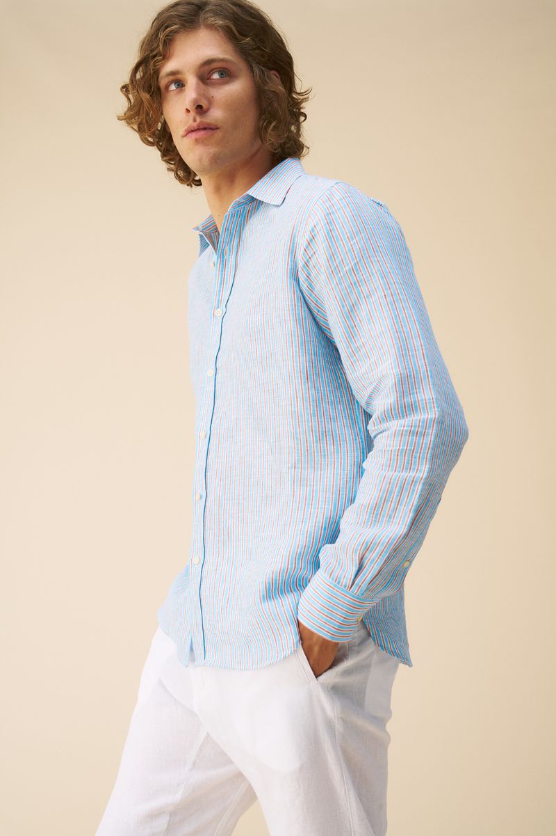 Man wearing a light blue striped linen shirt and white trousers against a neutral background