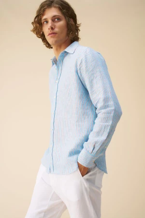 Man wearing a light blue striped linen shirt and white trousers against a neutral background
