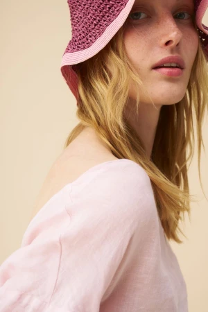 Close-up portrait of a woman wearing a pink woven bucket hat and light pink top against a neutral background.