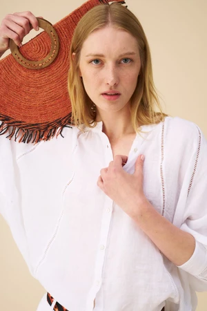A female model wearing a white linen shirt holds a textured orange straw handbag against a neutral studio background.