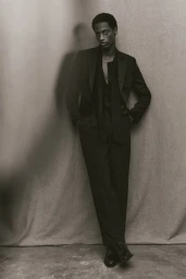 Model in a black suit leaning against a textured backdrop for an H and M project