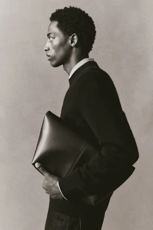 Profile portrait of a man wearing a dark crewneck sweater holding a dark leather clutch for H&M