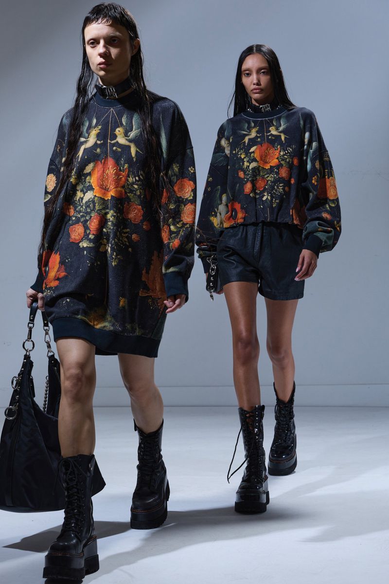 Two female models wearing patterned floral sweaters and black combat boots walking on a white seamless studio background