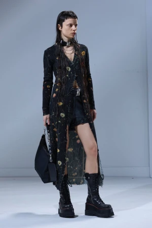 Model wearing a black floral cardigan and platform boots holding a black handbag against a white background