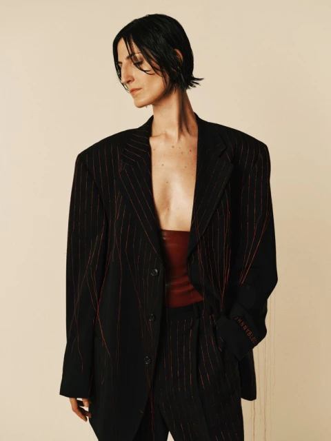 Adult woman in an oversized pinstripe suit and red top poses in a studio with a neutral background. Fashion editorial shot.