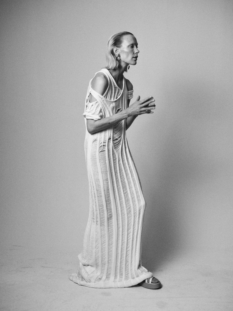 Elegant adult fashion model posing in a torn knit dress, neutral studio background, full shot, black and white, beauty and style.