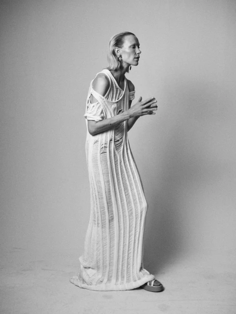 Elegant adult fashion model posing in a torn knit dress, neutral studio background, full shot, black and white, beauty and style.